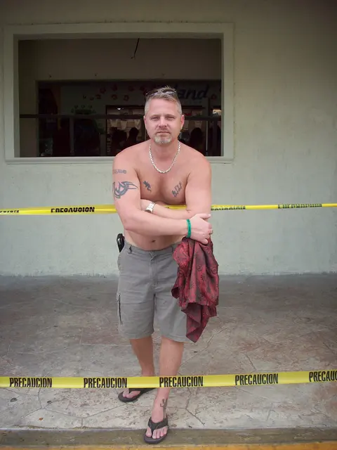 shirtless man in shorts standing outdoors behind caution tape