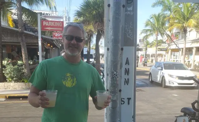 Man (John) holding two drinks on Key West street corner; fully clothed