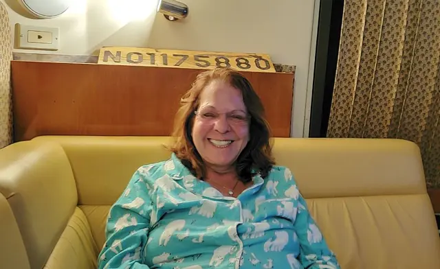 Woman (Lori) smiling on boat cabin couch wearing polar bear pajamas; fully clothed