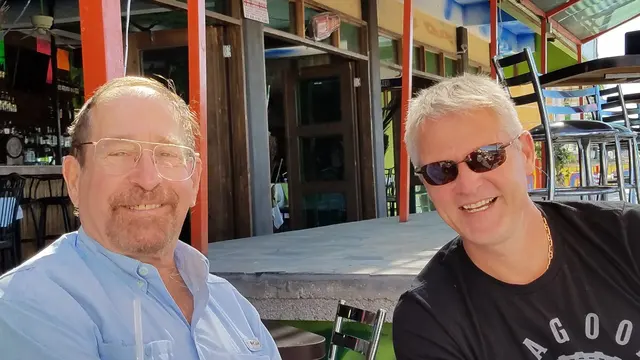 John and a friend sharing drinks at a colorful beachside bar