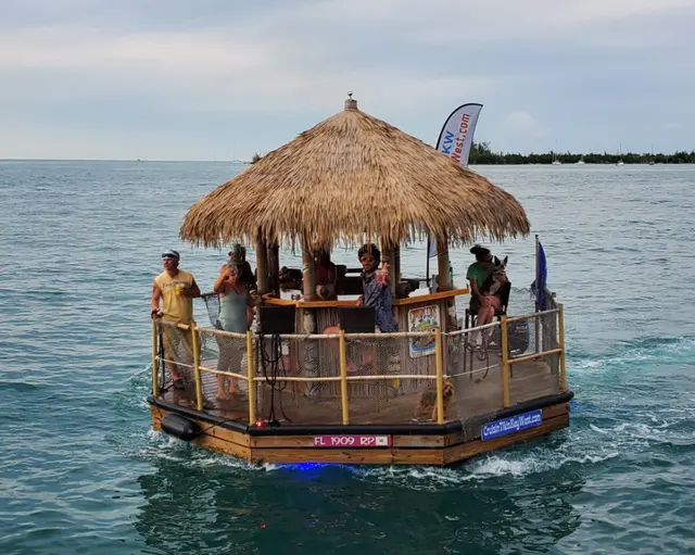 Tiki-roofed party boat with passengers and a dog on the water; fully clothed