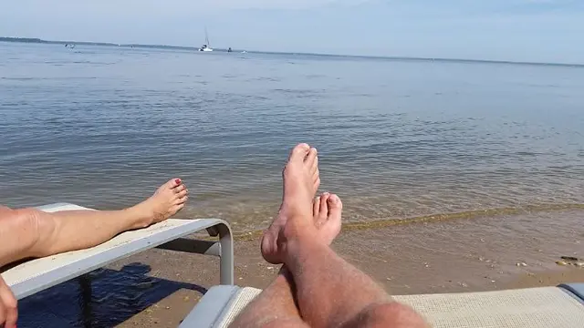 two people's feet relaxing on beach chairs by water
