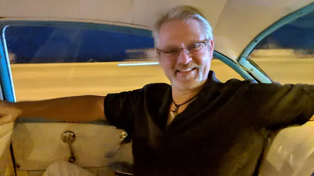 John riding through Havana by night in a classic car