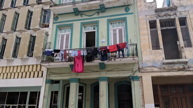 A weathered green building draped with laundry on the balcony