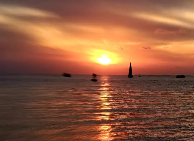 Sunset over ocean with silhouetted sailboat; scenery