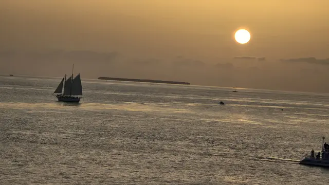 A sailing catamaran glides past as the sun dips low.
