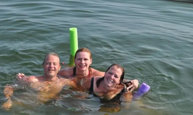 three people swimming in water with pool noodle