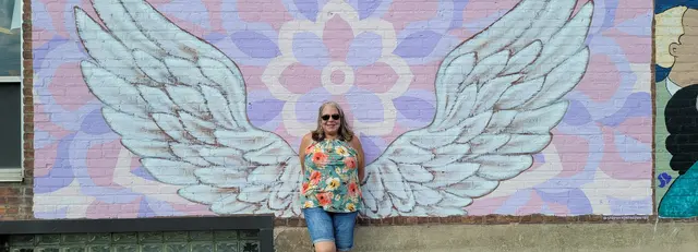 Lori posing with an angel wings mural downtown