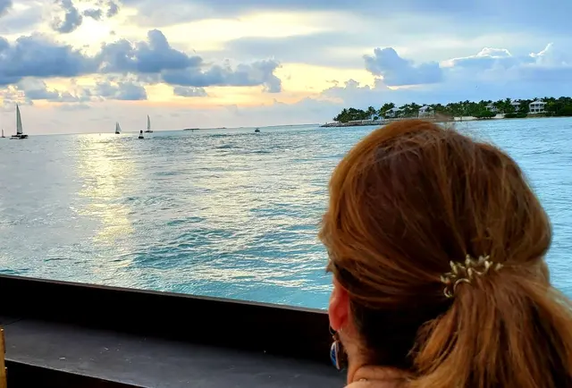 Woman (Lori) from behind watching sunset over water with sailboats; fully clothed