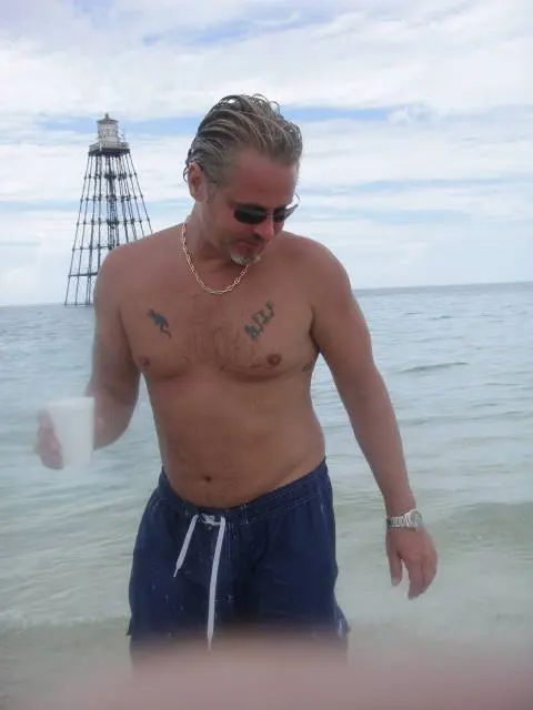 shirtless man standing in water near lighthouse