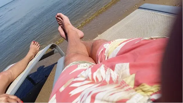 two people's feet relaxing on beach chairs by water