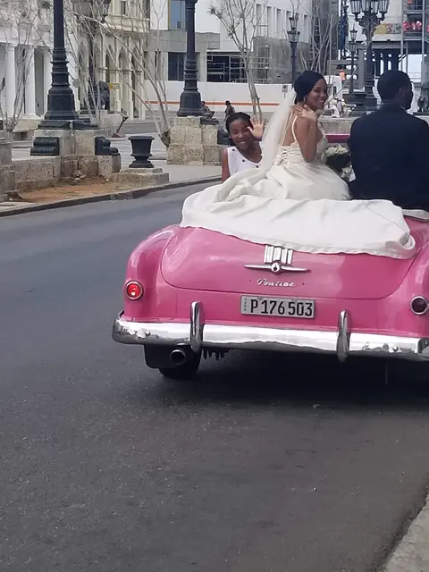 A bride and groom posing in a pink classic Pontiac