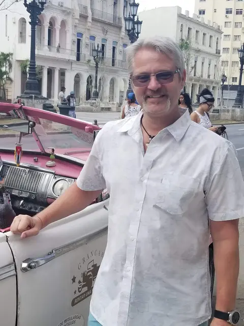 John smiling on the Malecon with a classic pink taxi