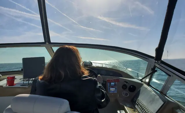 Woman (Lori) from behind driving boat on sunny open water; fully clothed
