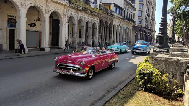 A bright pink classic convertible cruising past colonial arcades