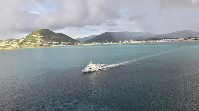 A charter boat cruising past St. Maarten's green hills and turquoise bay.