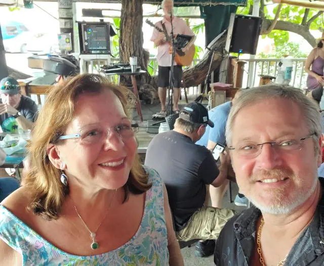 John and Lori selfie at outdoor bar with live musician; both fully clothed