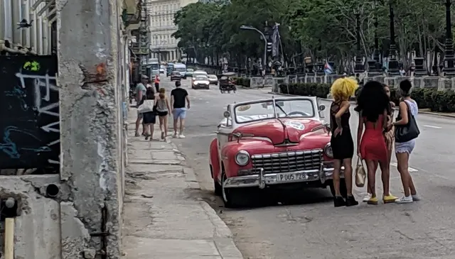 Locals gathered around a vintage red convertible in the street