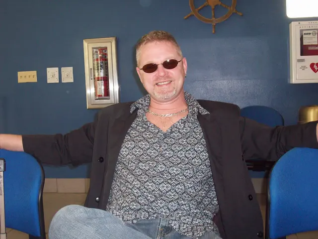 man seated indoors sunglasses smiling